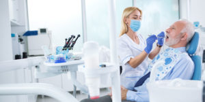 Elderly male dental implant patient undergoing exam with female hygienist wearing surgical mask