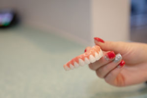 Female hand with red and sparkly nail polish holding zirconia full arch dental prosthesis