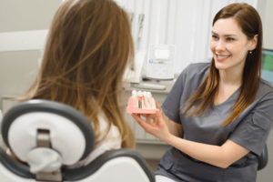a happy dentist showing her patient a dental implant model before her dental implant surgery.