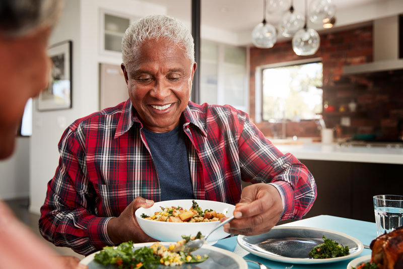 a patient smiling over his bowl of food at the dinner table because he has had a comprehensive dental implant procedure.